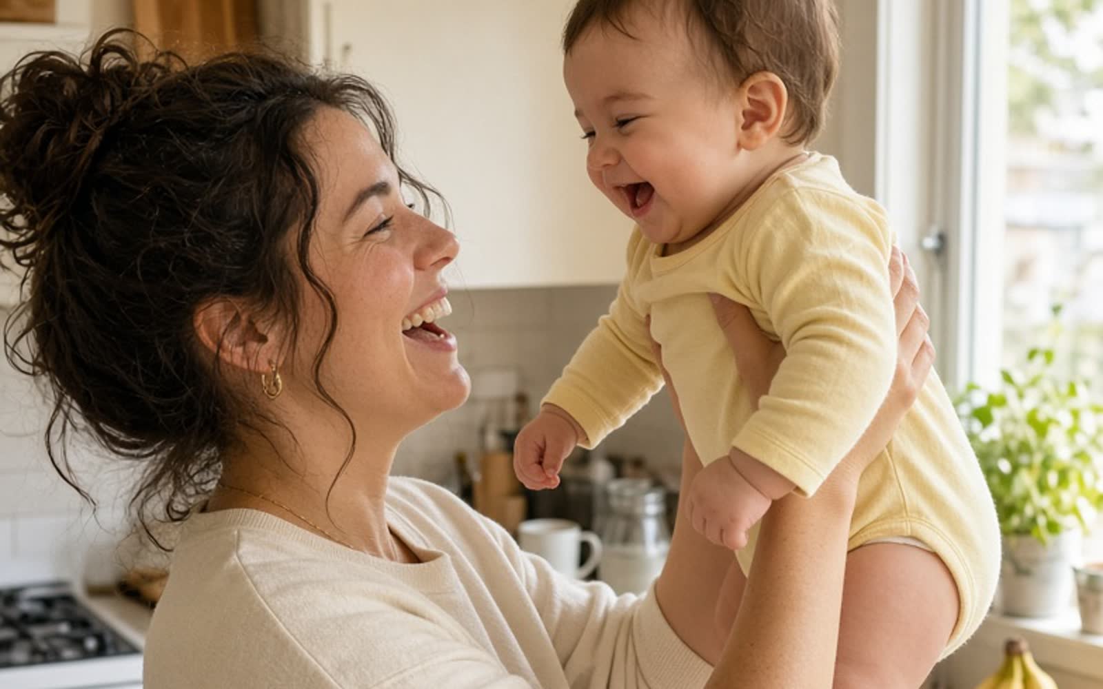 A laughing mother holding her baby up in a sunny kitchen